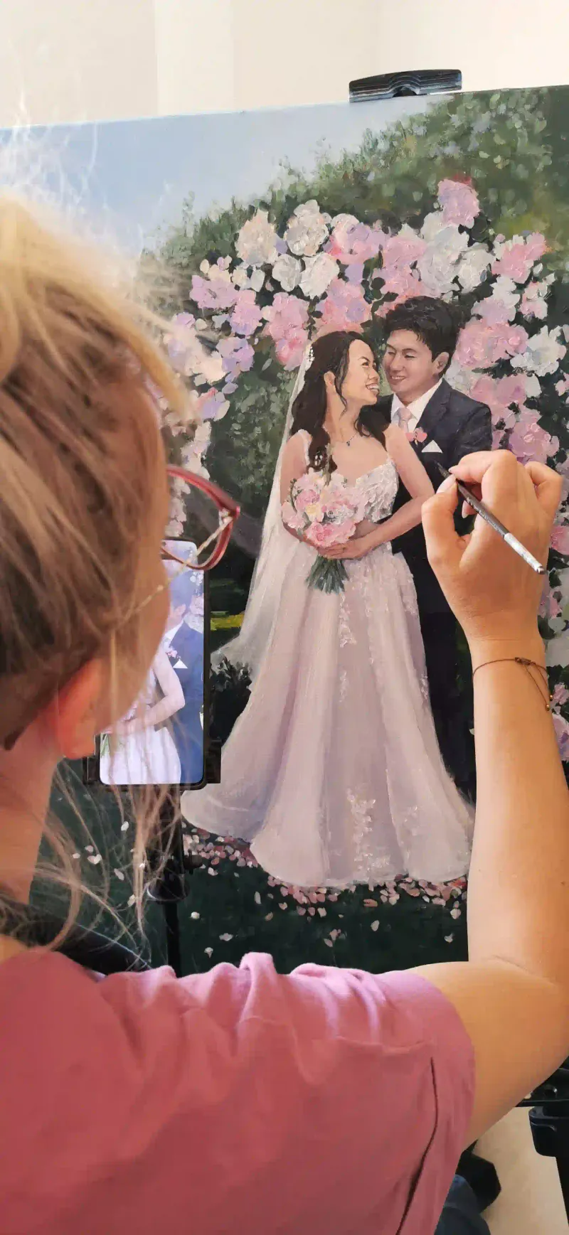 Live wedding painter Marta at her easel capturing a couple beneath a floral arch